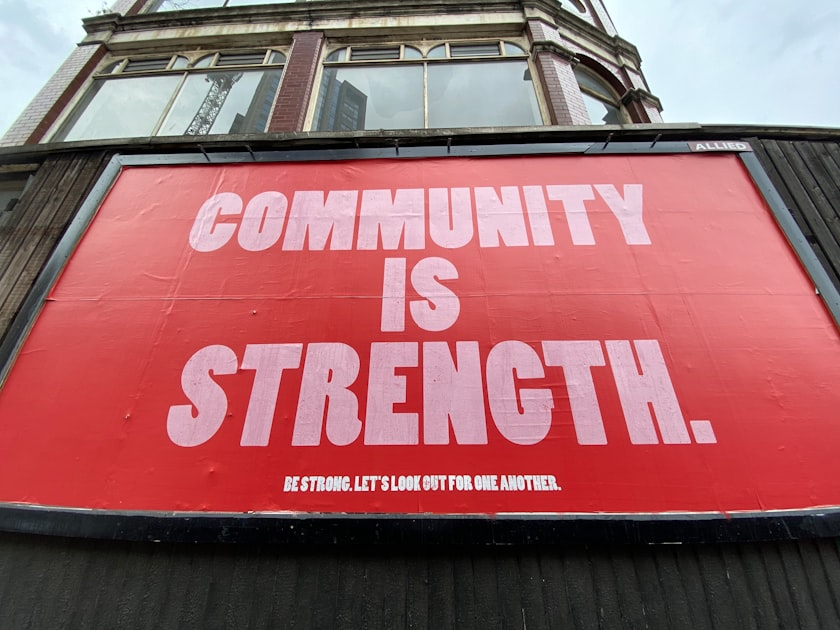 Large red mural on a building facade with bold white text reading, “COMMUNITY IS STRENGTH.” and smaller text below, “BE STRONG. LET’S LOOK OUT FOR ONE ANOTHER.” to depict community preparedness in rochester